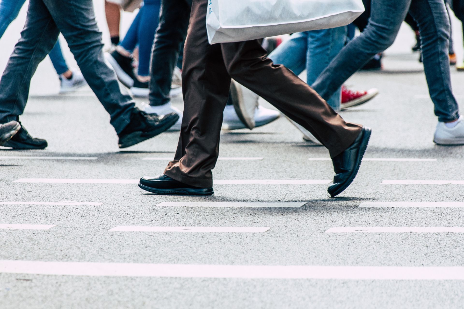 The lower half of several pedestrians walking across a painted white crosswalk on an asphalt city street.