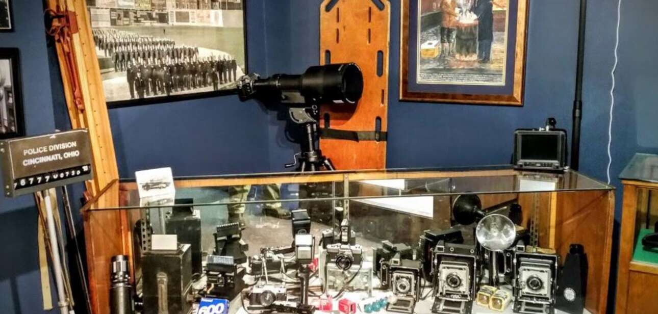 A display case at the Greater Cincinnati Police Museum featuring historical law enforcement artifacts, including vintage cameras, radios, and a tabletop siren.
