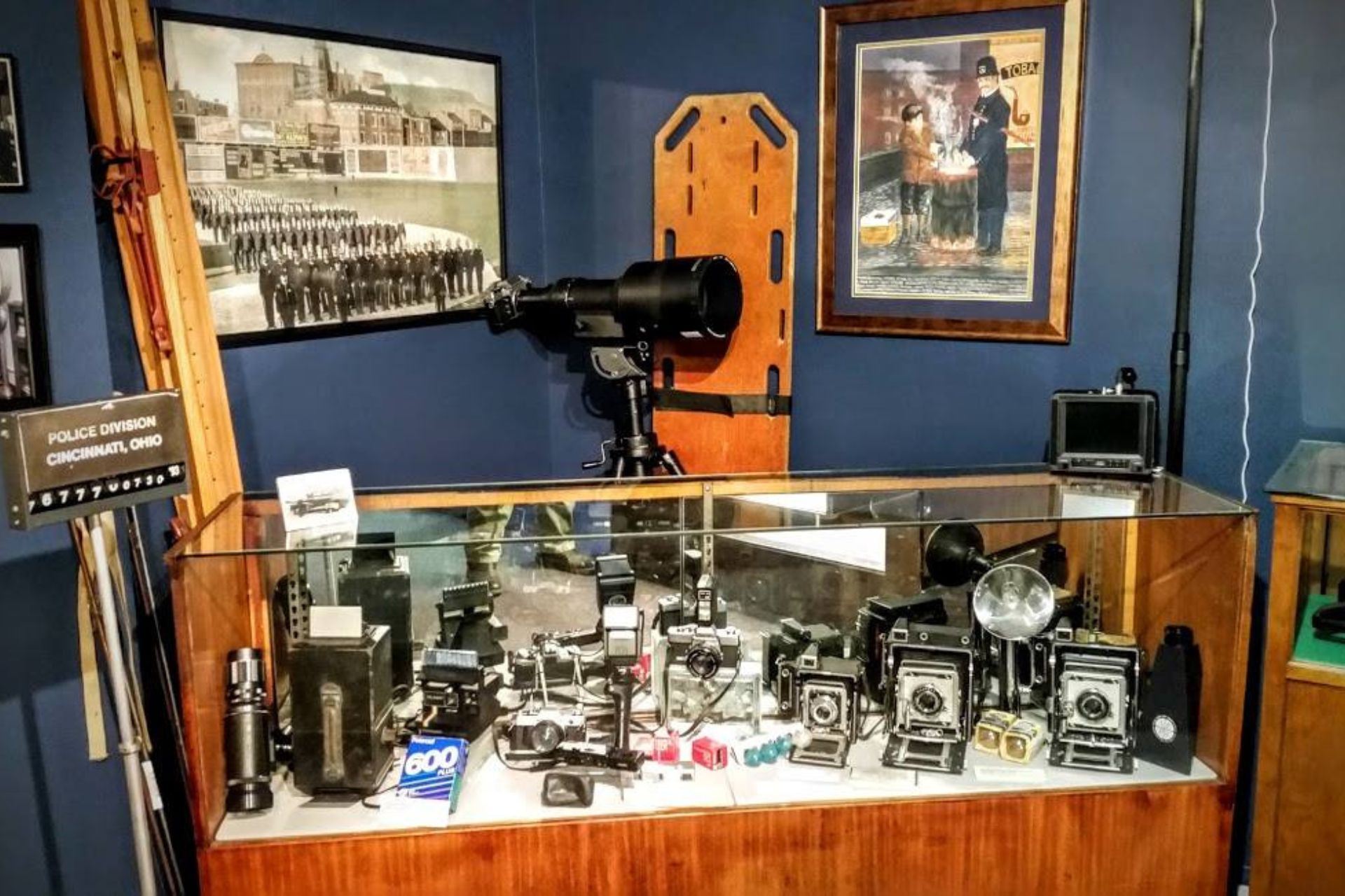 A display case at the Greater Cincinnati Police Museum featuring historical law enforcement artifacts, including vintage cameras, radios, and a tabletop siren.