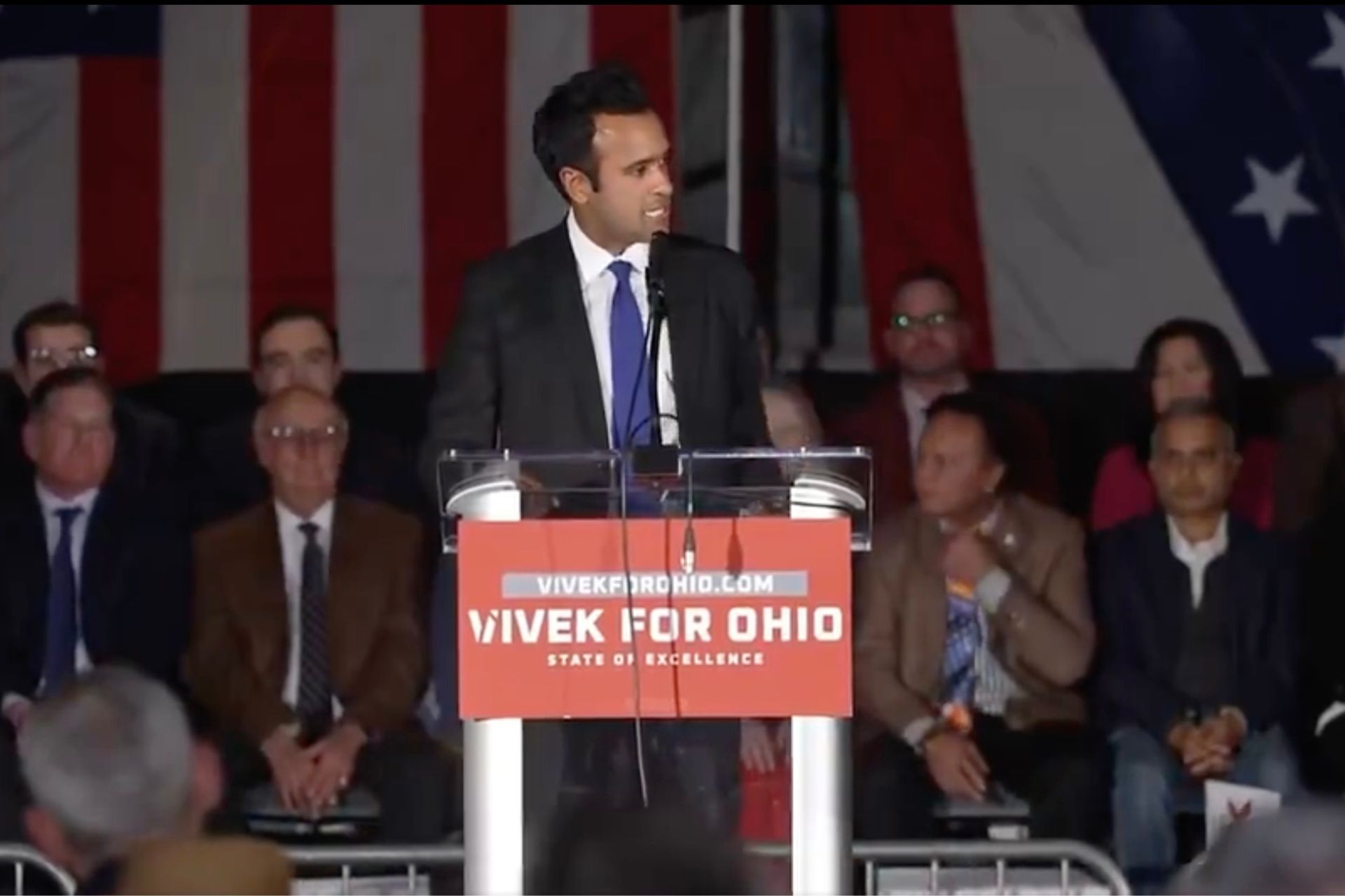 Vivek Ramaswamy speaking at a podium with a "Vivek for Ohio" sign during a 2026 gubernatorial campaign event.