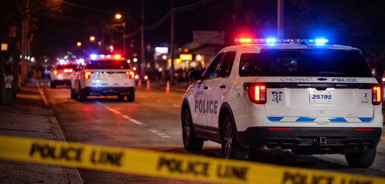Cincinnati police vehicles block a street at night with emergency lights active following the Riverfront Live shooting in the East End