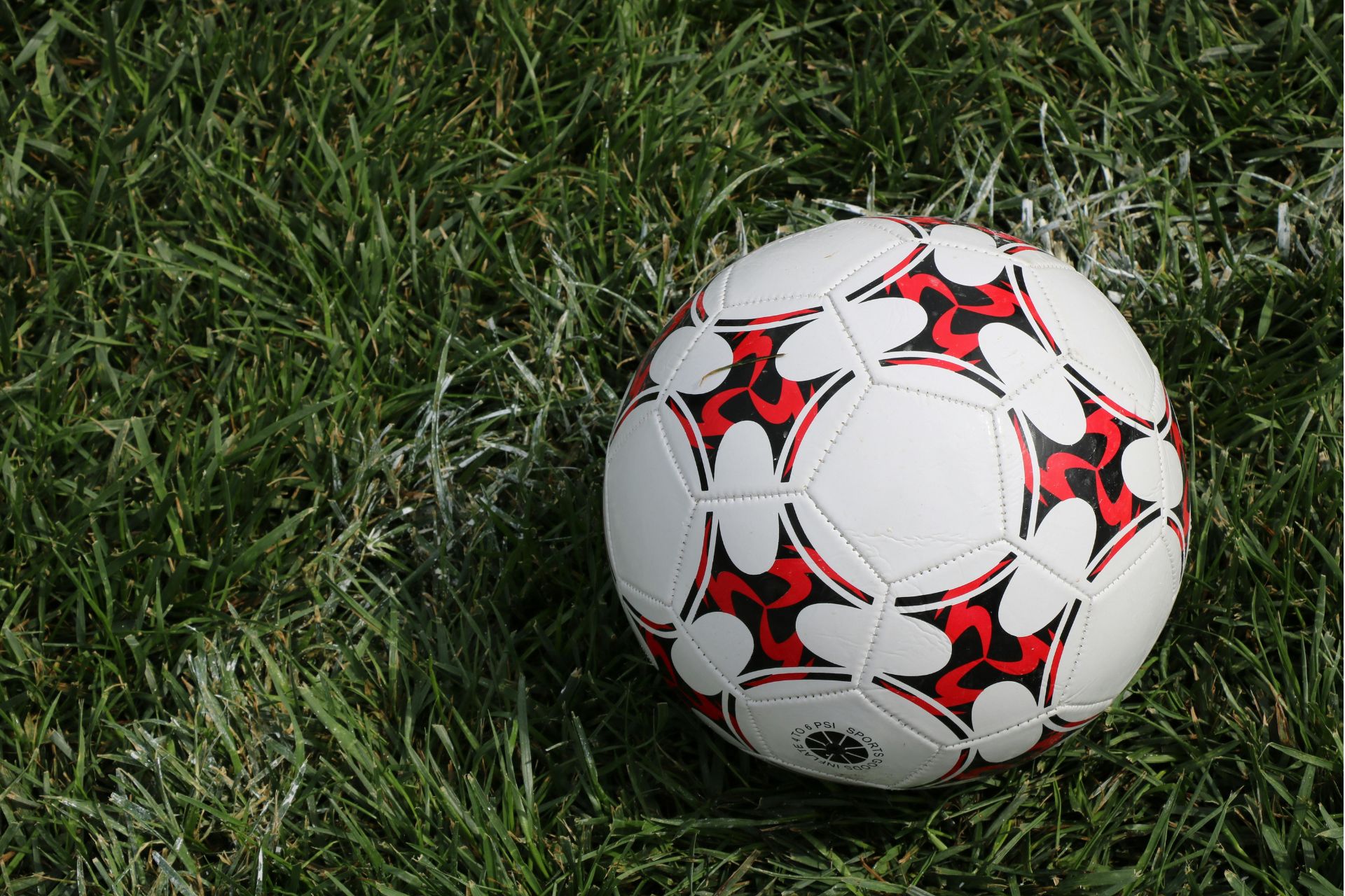 A red and white soccer ball sits on a green grass pitch.