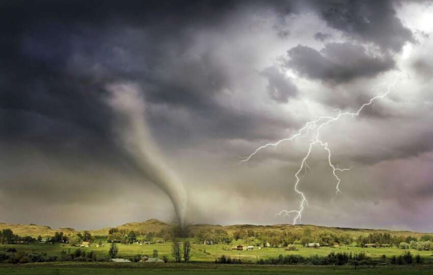 A dark funnel cloud touches down in a rural green field under ominous storm clouds with visible lightning strikes.