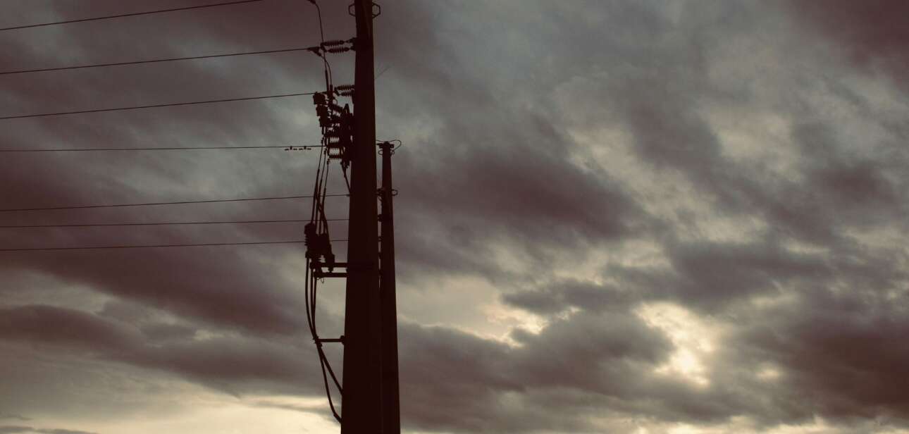 Silhouette of a utility pole and power lines against a dark, stormy sky.