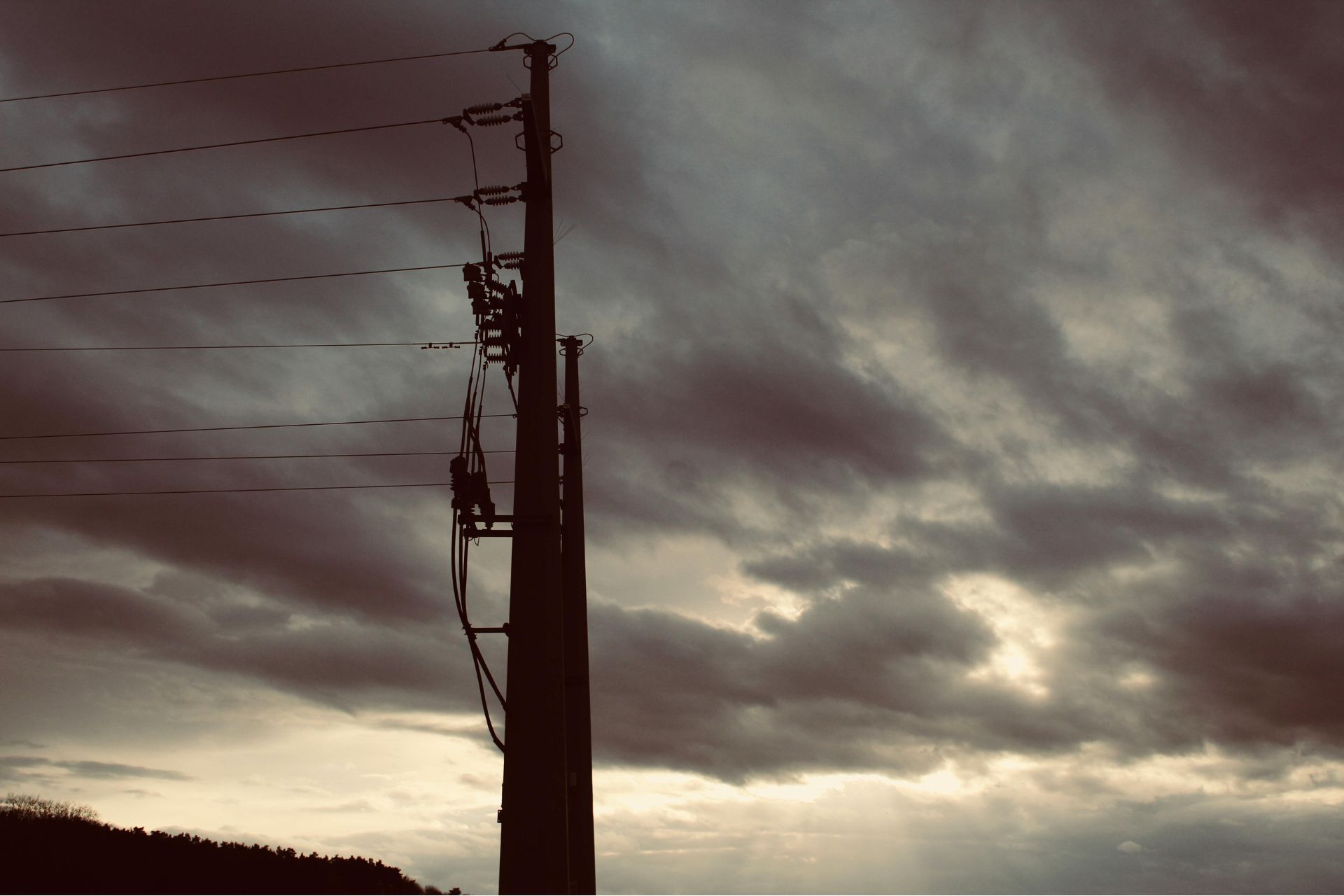 Silhouette of a utility pole and power lines against a dark, stormy sky.