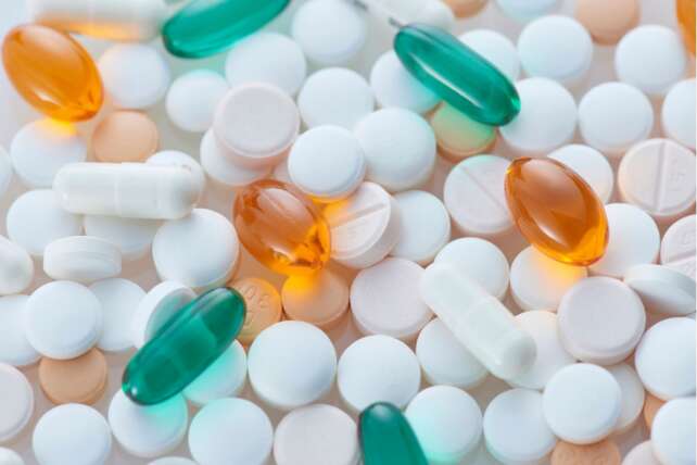A close-up view of assorted white round prescription pills and green and orange capsules scattered together.