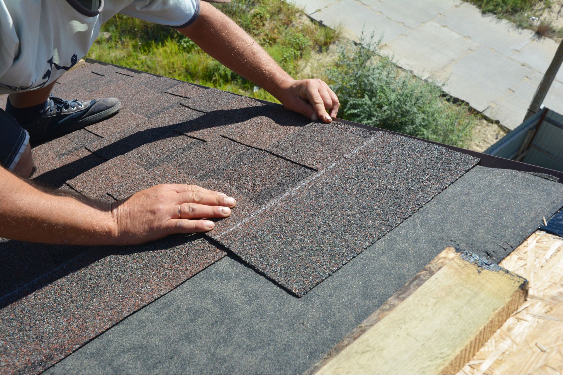 A close-up of a contractor's hands installing new dark gray shingles on a residential roof in Cincinnati.