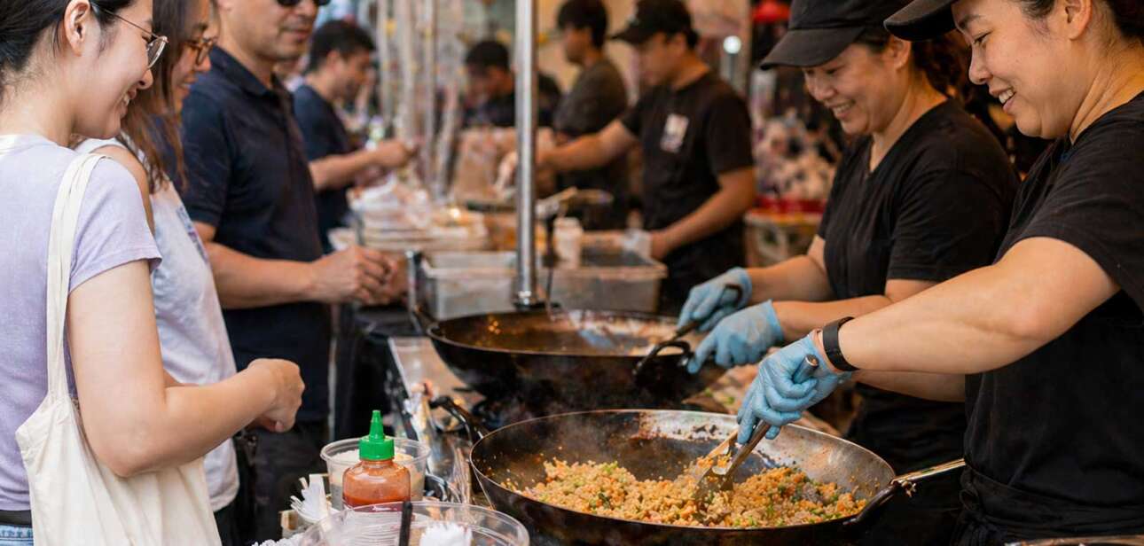 Asian food vendors cooking fried rice in large woks while a line of customers waits at a busy festival booth