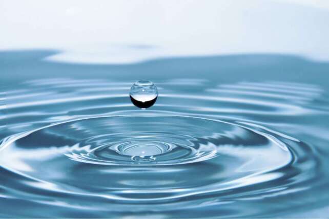 A single water drop creating concentric ripples on a blue surface for Cincinnati's canned water announcement.