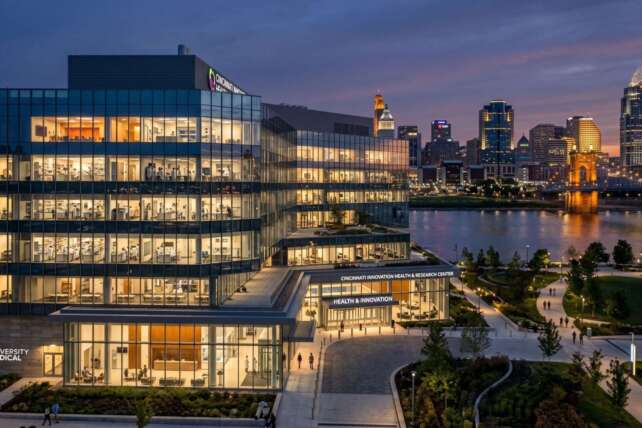 State-of-the-art glass healthcare and research facility in Cincinnati with the city skyline at dusk.