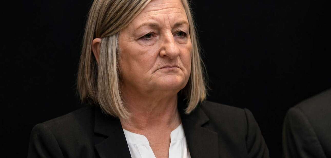 Close-up of Teresa Theetge with a tense expression, wearing a black blazer and white blouse against a dark background following her firing as Cincinnati police chief