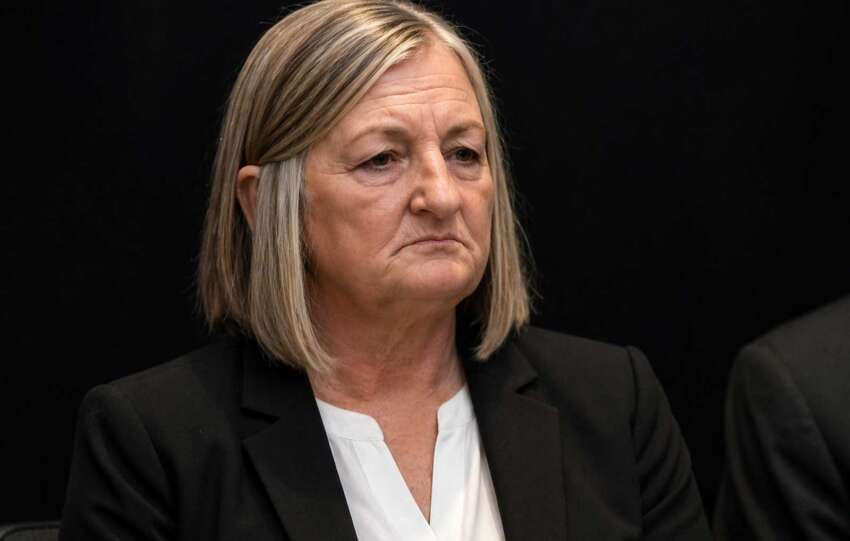 Close-up of Teresa Theetge with a tense expression, wearing a black blazer and white blouse against a dark background following her firing as Cincinnati police chief