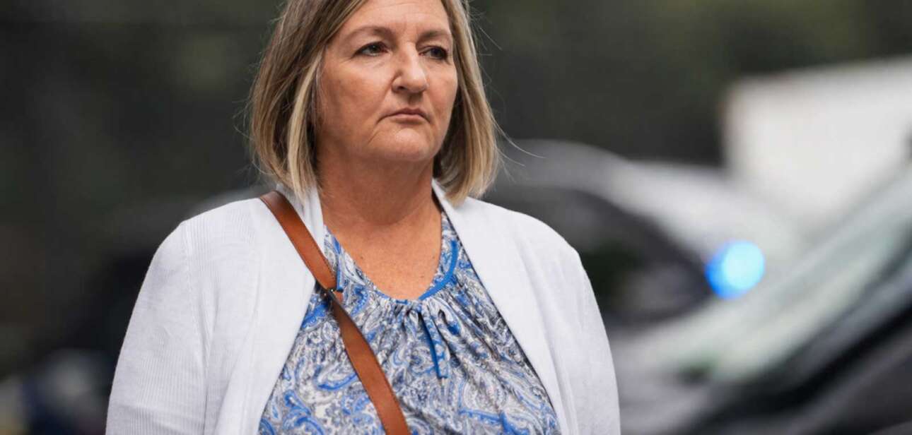 Teresa Theetge walking in a hallway wearing a white blazer and blue patterned blouse during a public appearance