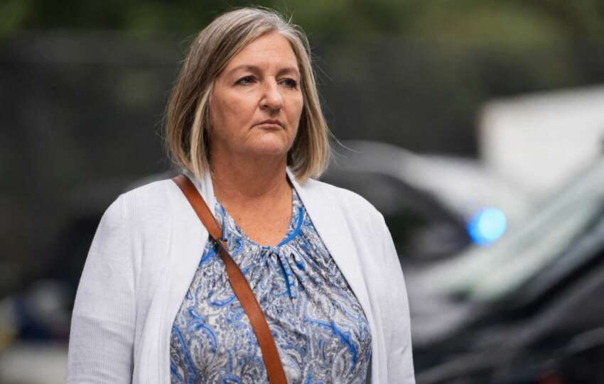 Teresa Theetge walking in a hallway wearing a white blazer and blue patterned blouse during a public appearance