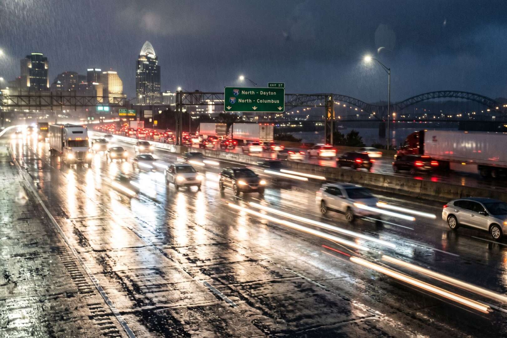 Cincinnati rain slicked highway at night with heavy traffic, glowing headlights, and the city skyline in the background.