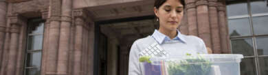 Woman in her 30s carrying a box of belongings outside Cincinnati City Hall after a job loss