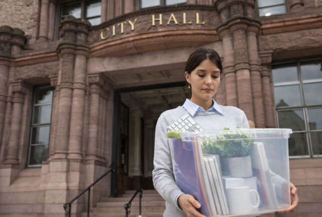 Woman in her 30s carrying a box of belongings outside Cincinnati City Hall after a job loss