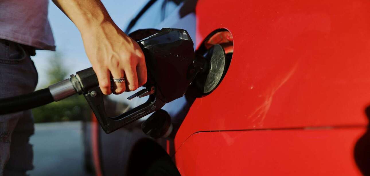 A person pumping gasoline into a red car at a gas station, symbolizing rising fuel costs in Cincinnati.