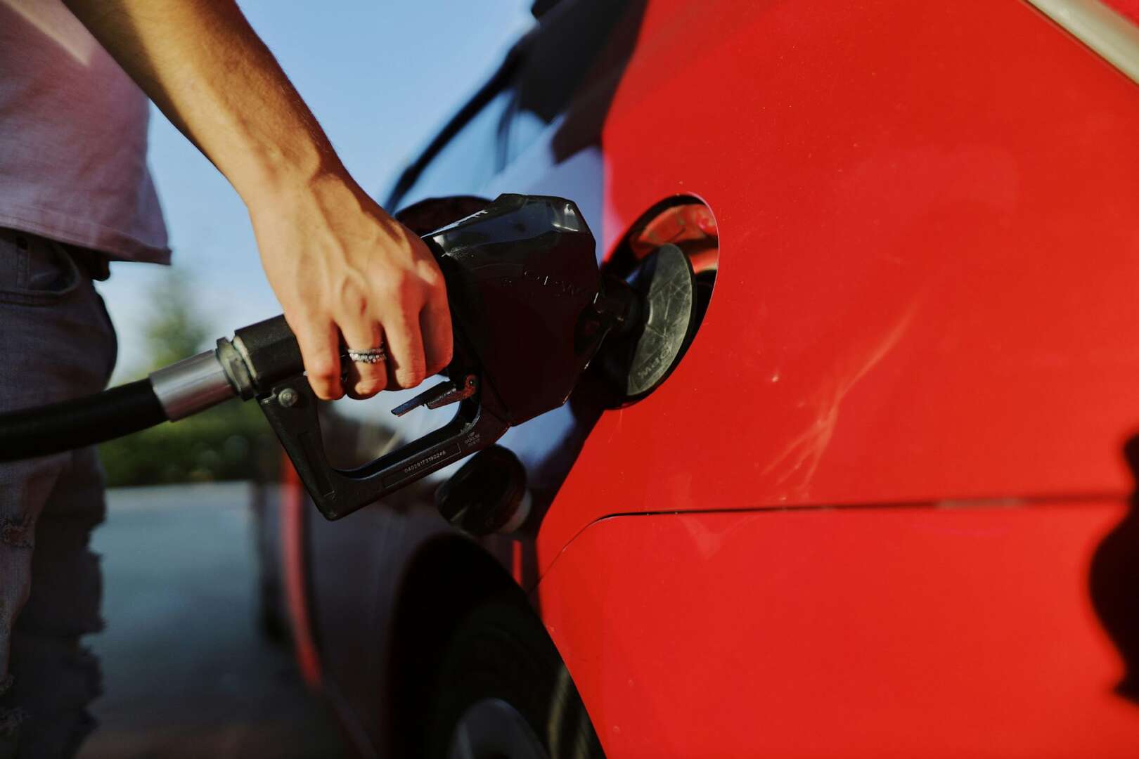 A person pumping gasoline into a red car at a gas station, symbolizing rising fuel costs in Cincinnati.
