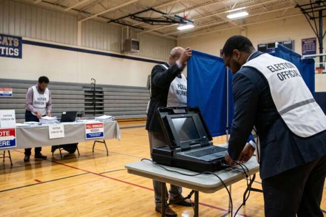 Poll workers set up electronic voting machines and organize voter check-in tables inside a school gymnasium ahead of the Ohio primary election.