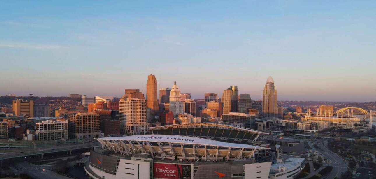 Aerial view of a large football stadium in downtown Cincinnati with surrounding city skyline at sunset.