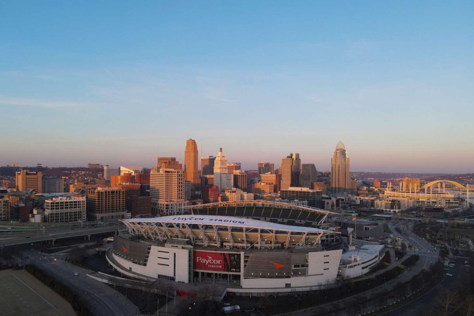 Aerial view of a large football stadium in downtown Cincinnati with surrounding city skyline at sunset.