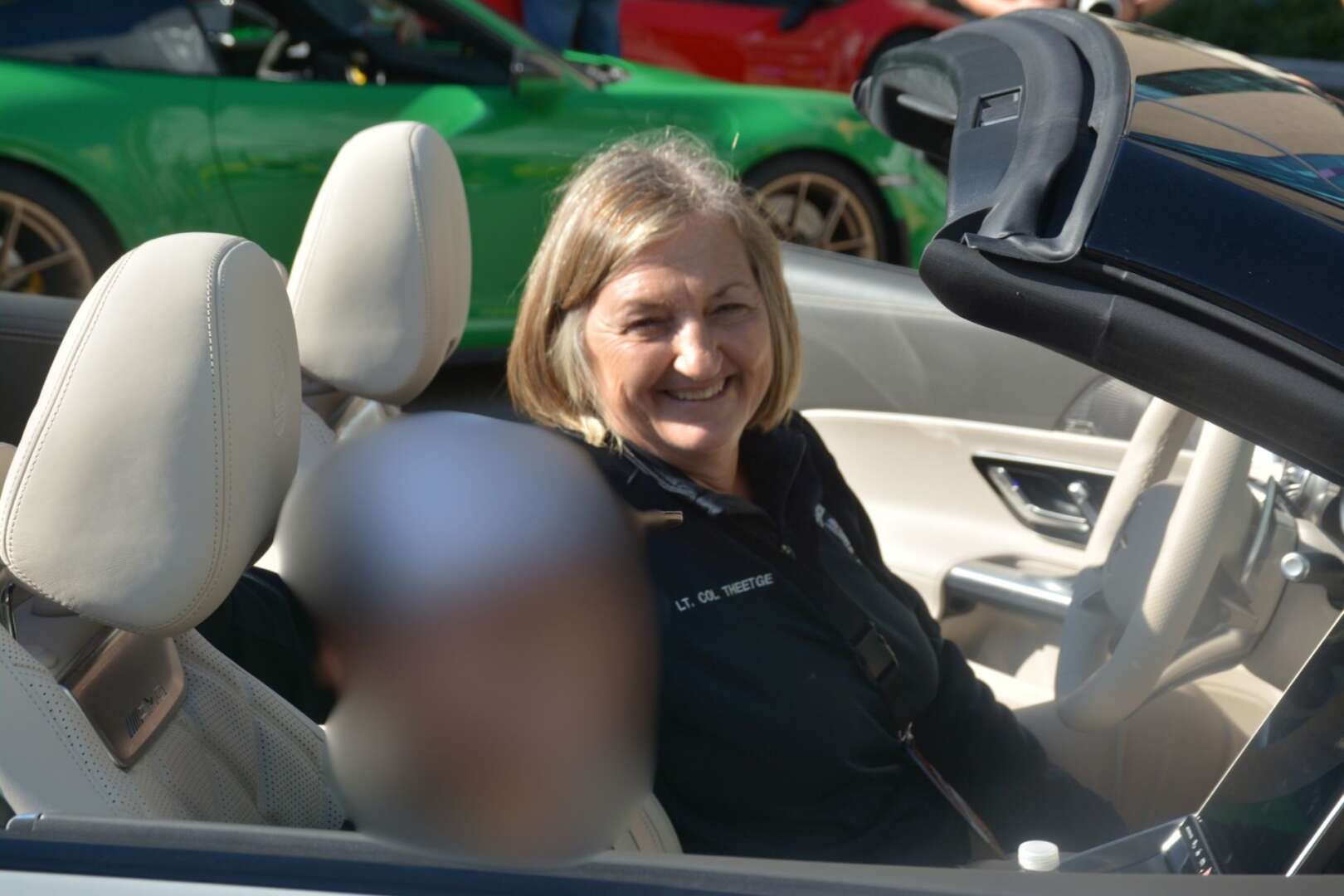 Cincinnati Police Chief Teresa Theetge smiling in the passenger seat of a car during an event.