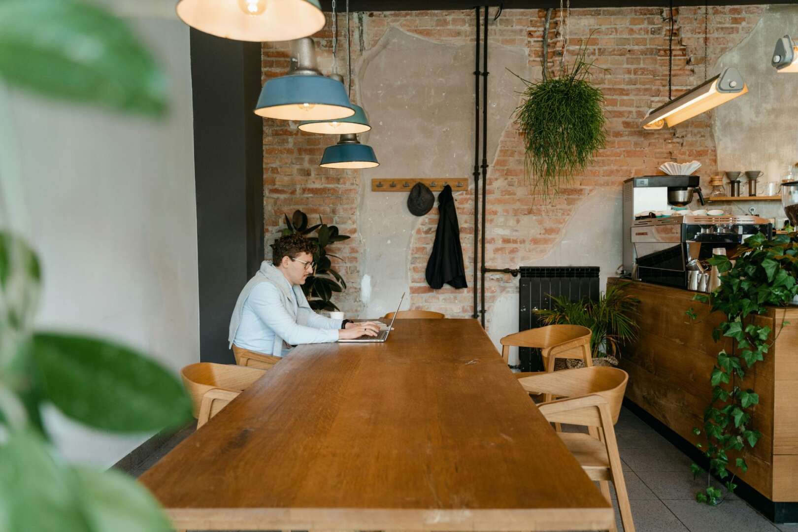 A young professional works on a laptop at a large wooden table inside a modern coffee shop, representing the growth of remote work and the gig economy in Cincinnati.