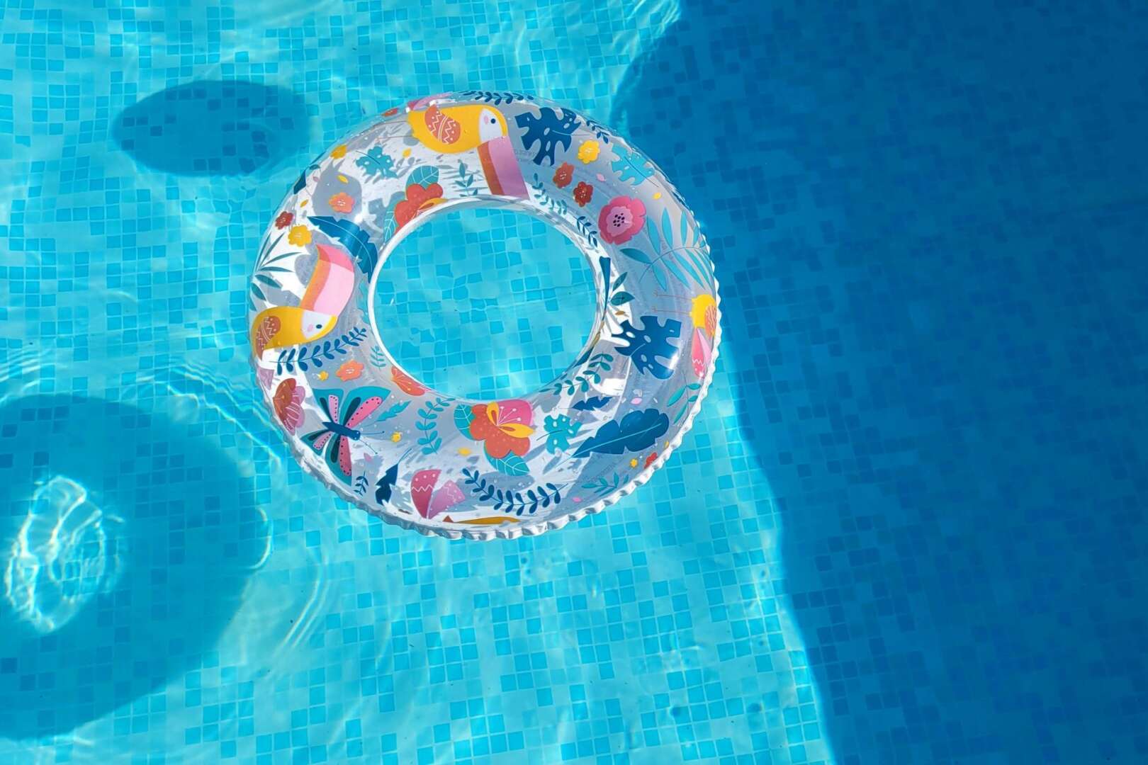 A colorful, patterned inflatable pool ring floating in bright blue water, illustrating the early opening of Cincinnati public pools.