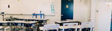 An empty, modern classroom at Cincinnati Public Schools with rows of white desks and chairs, a whiteboard, and an American flag, representing potential budget cuts or school closures.