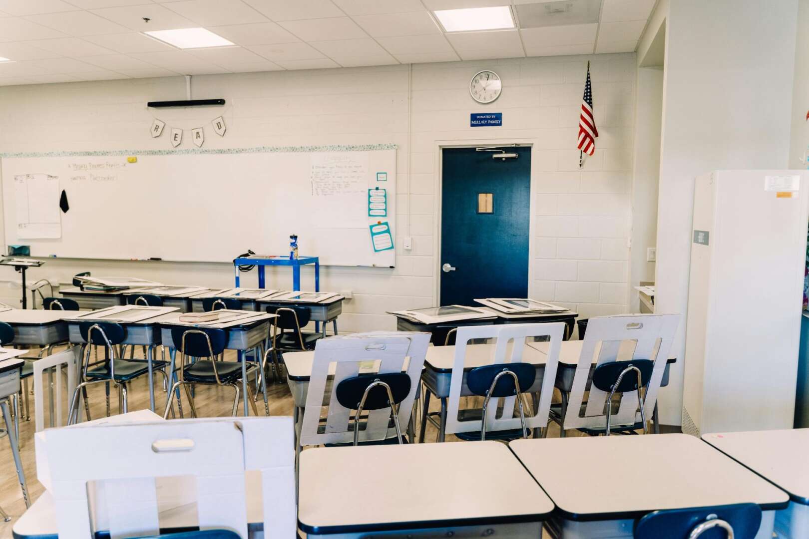 An empty, modern classroom at Cincinnati Public Schools with rows of white desks and chairs, a whiteboard, and an American flag, representing potential budget cuts or school closures.