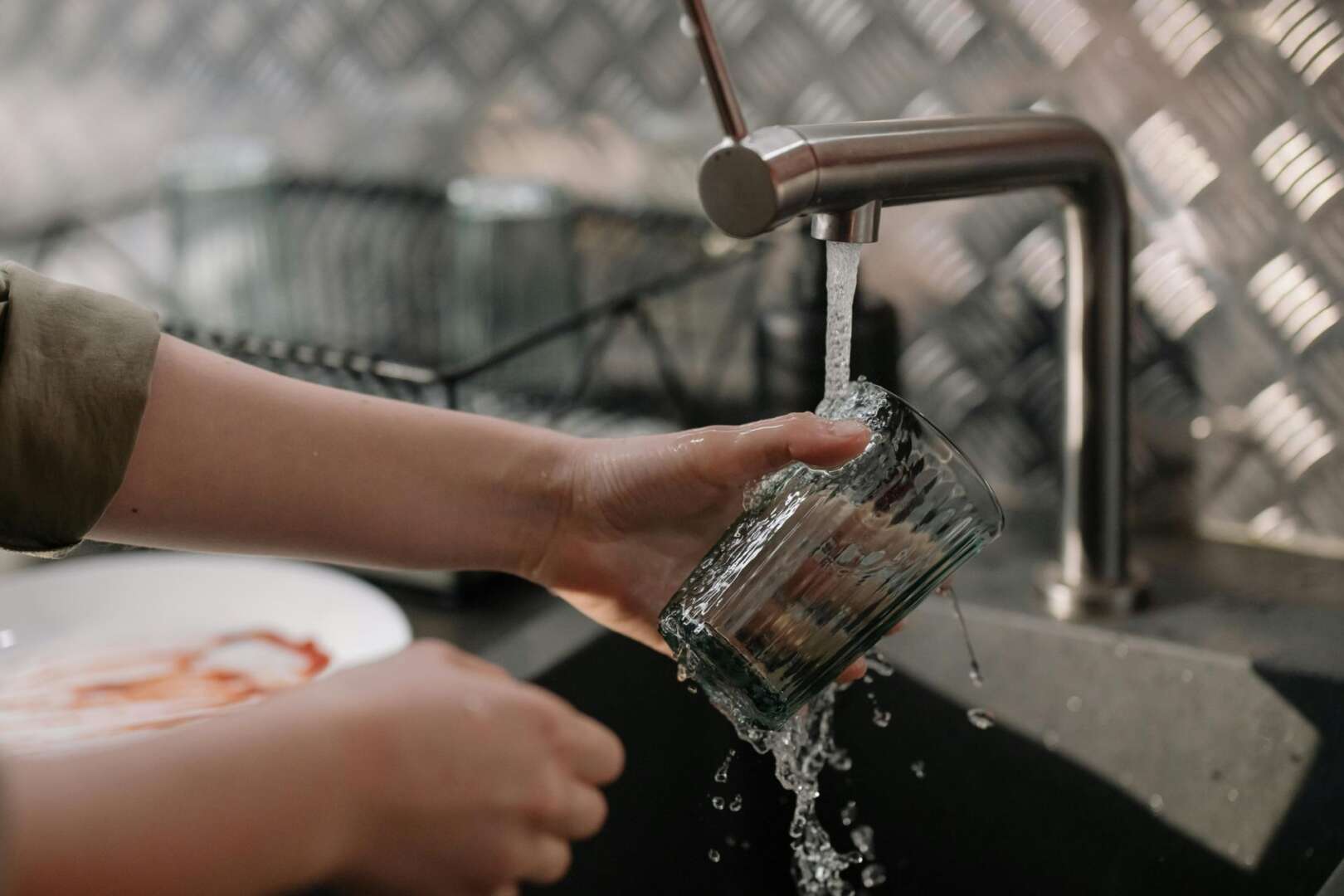 A person rinsing a glass under running tap water at a kitchen sink, representing residential water usage amidst 2026 Cincinnati water bill increases.