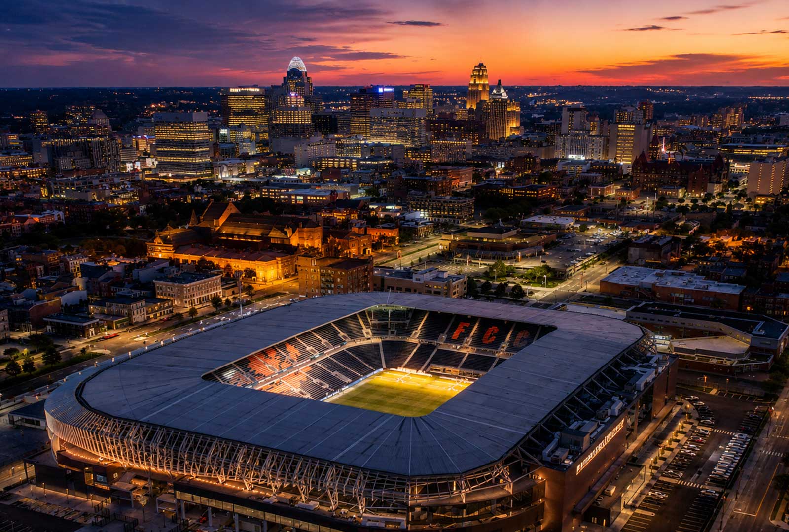 Aerial sunset view of TQL Stadium and downtown Cincinnati from the West End, with the FC Cincinnati stadium glowing beneath the city skyline at dusk.