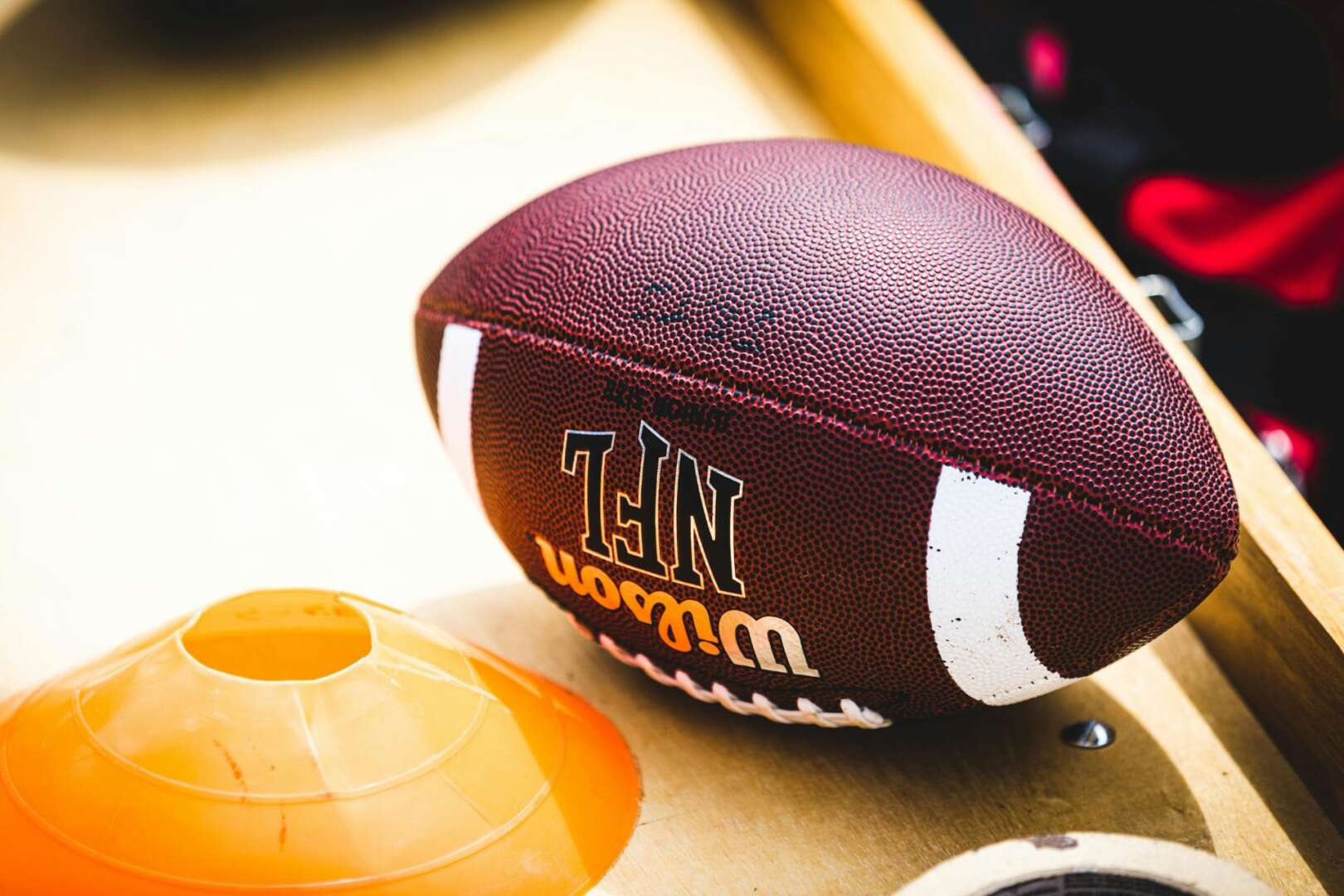 A Wilson NFL football sitting next to an orange practice cone on a wooden surface, representing NFL Draft preparations in Cincinnati and Minnesota.