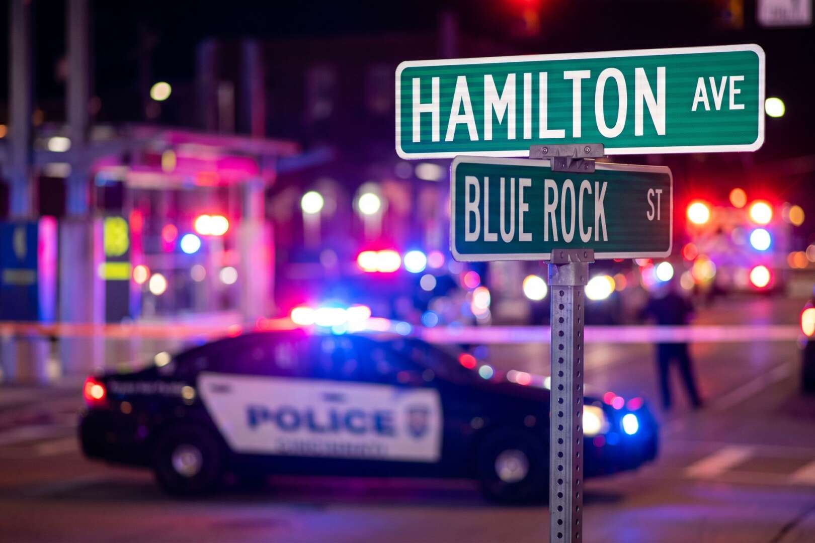 Police cruiser with flashing lights blocking the intersection of Hamilton Avenue and Blue Rock Street behind yellow crime scene tape in Northside, Cincinnati.