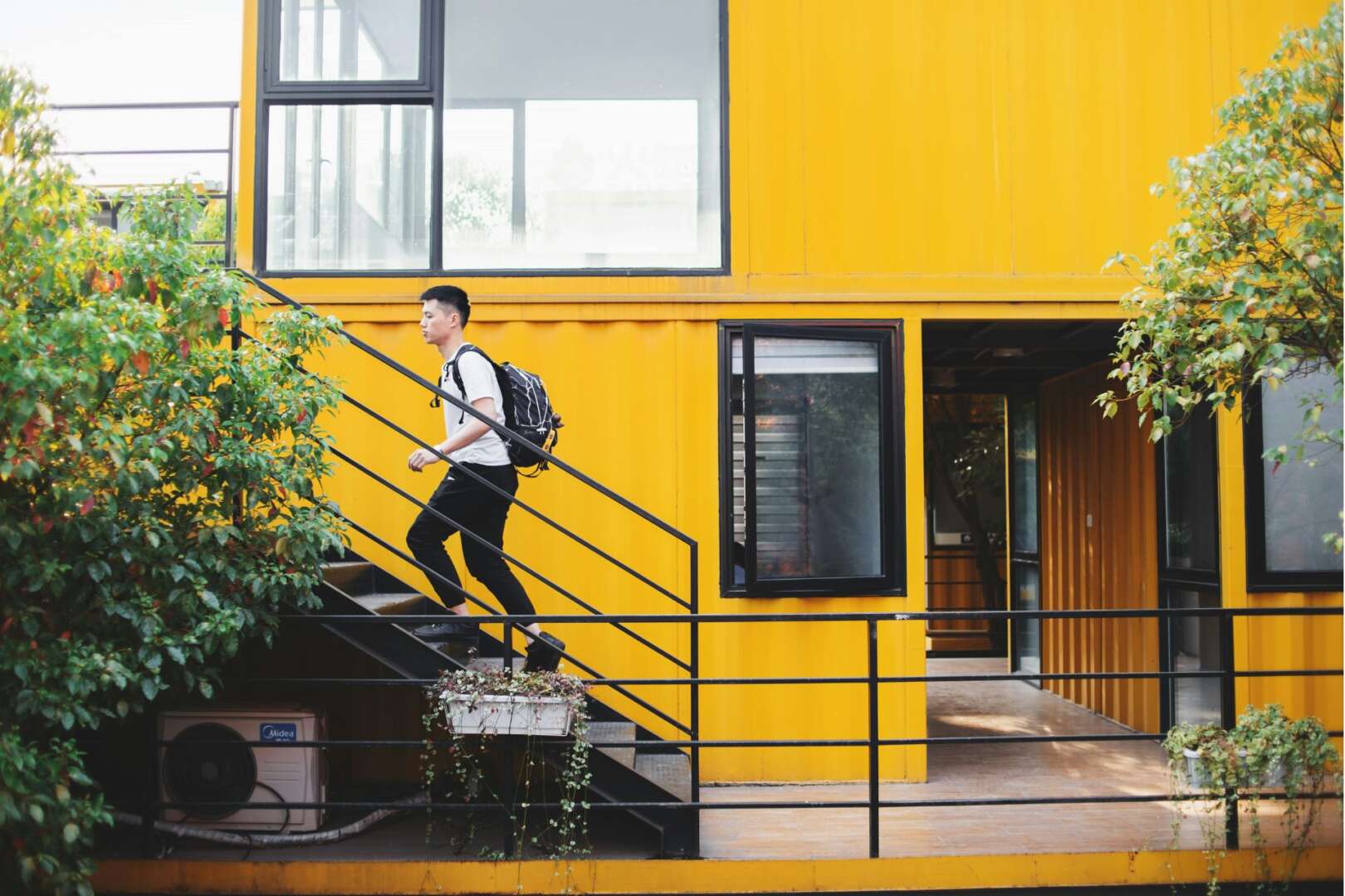 A student walks up the exterior stairs of a modern yellow off-campus apartment building, illustrating the student housing Cincinnati 2026 demand.