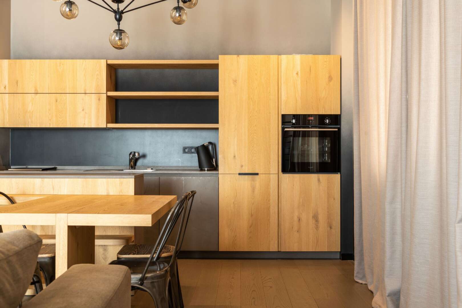 Modern kitchen with light wood cabinets, dark countertops, and a dining area, showcasing an apartment renovation.