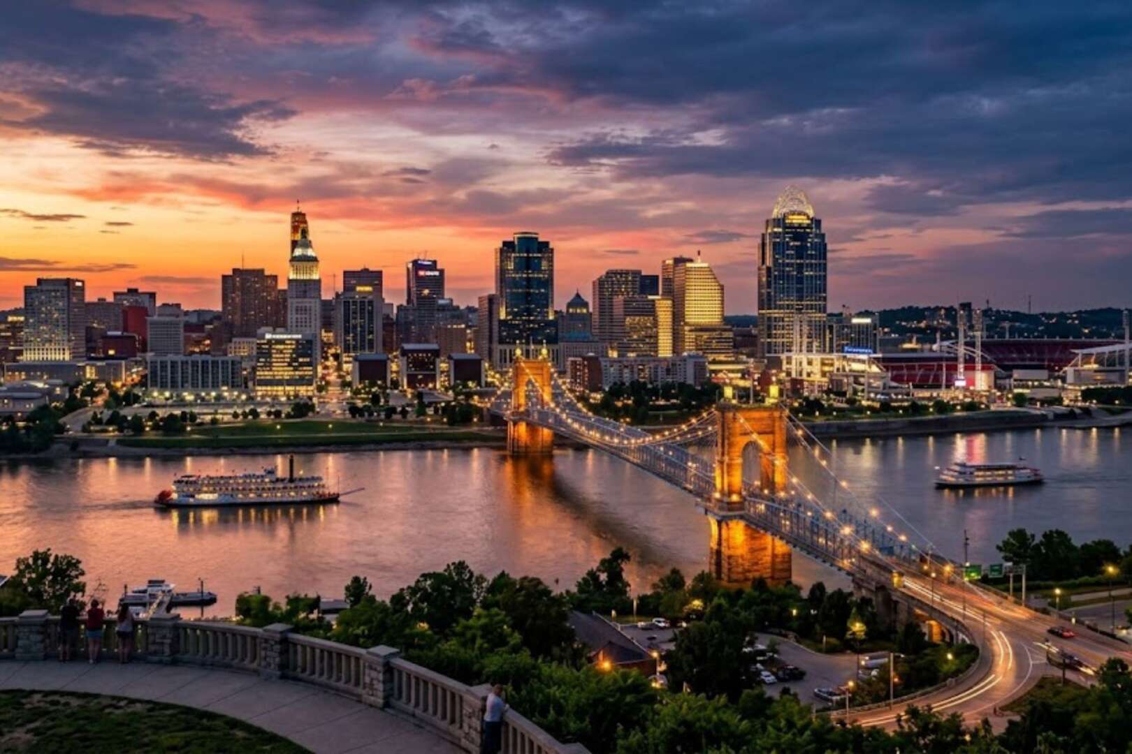 anoramic view of the Cincinnati skyline and the illuminated John A. Roebling Suspension Bridge over the Ohio River at sunset.