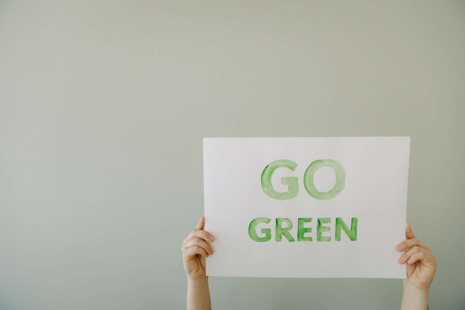 Two hands holding up a white sign with green lettering that reads "GO GREEN".