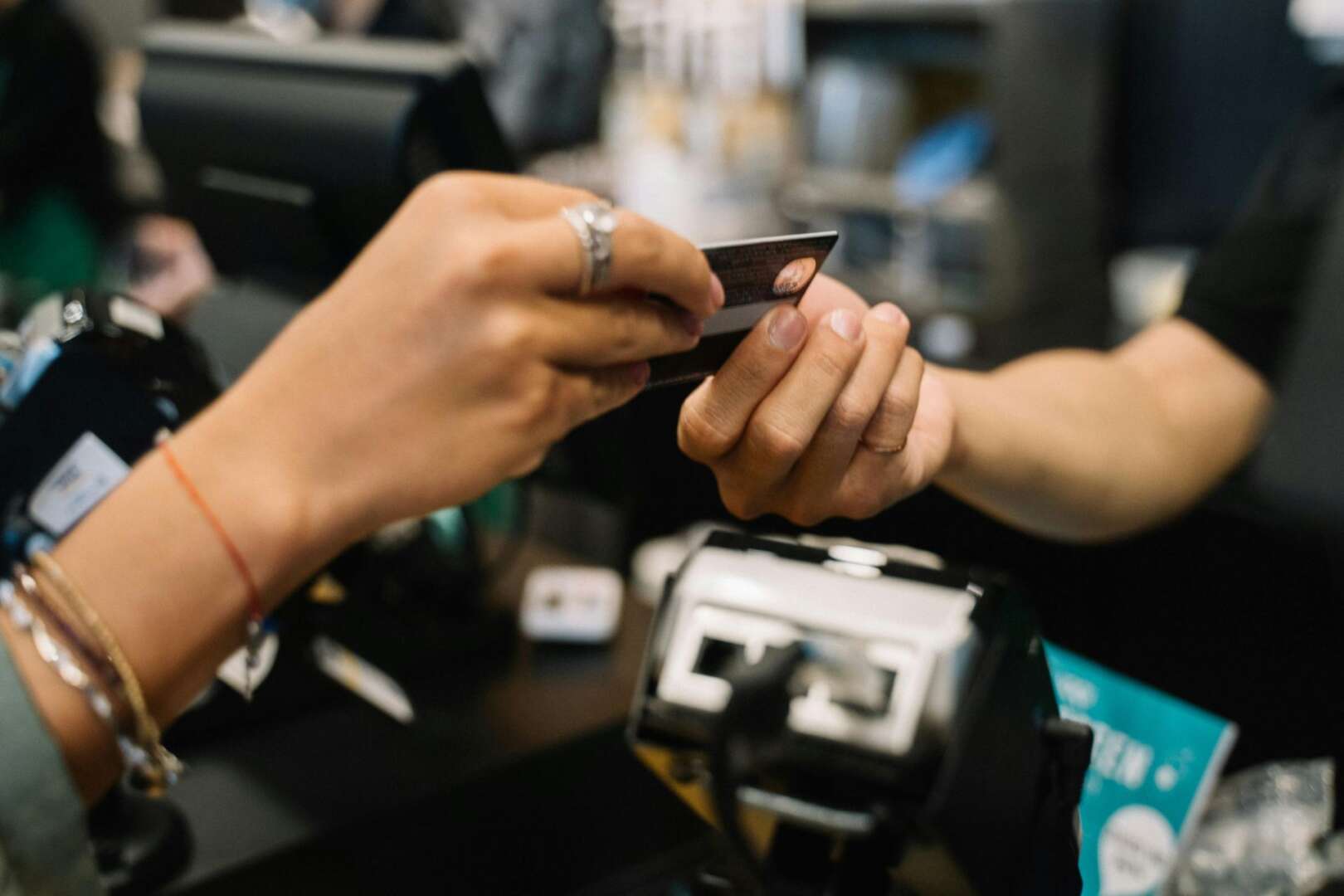 Close-up of a customer's hand giving a credit card to a retail cashier at a store checkout counter.