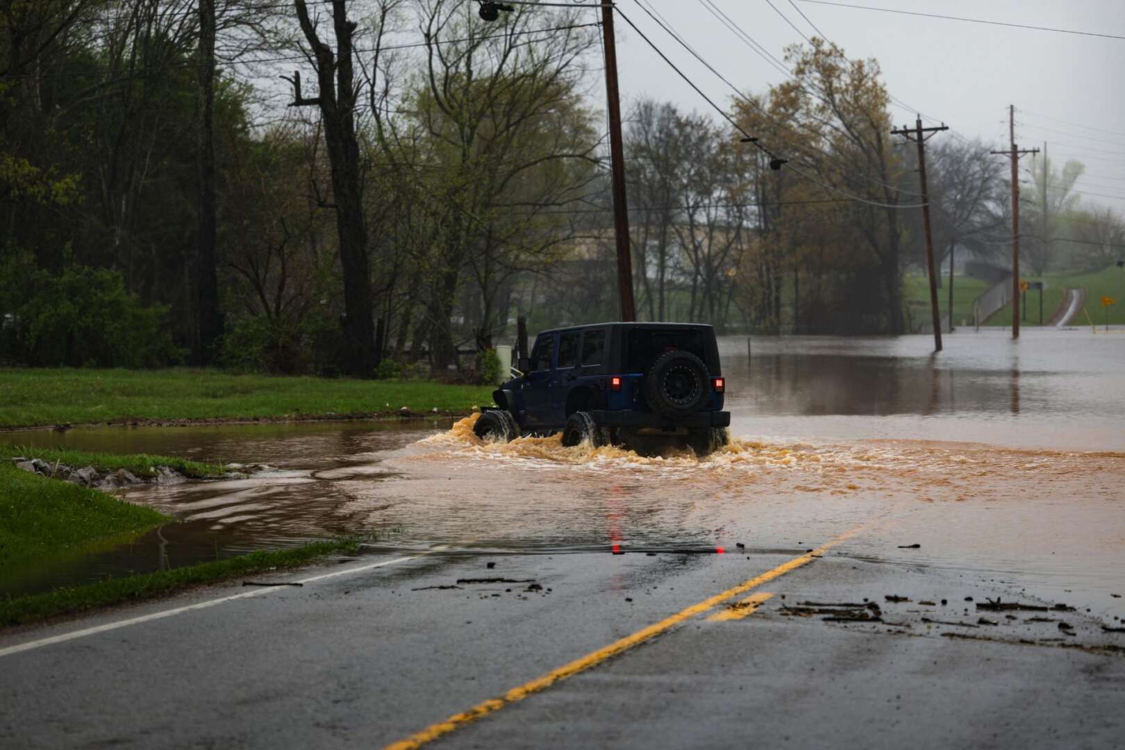 A black SUV partially submerged while attempting to drive through deep floodwaters on a residential street.