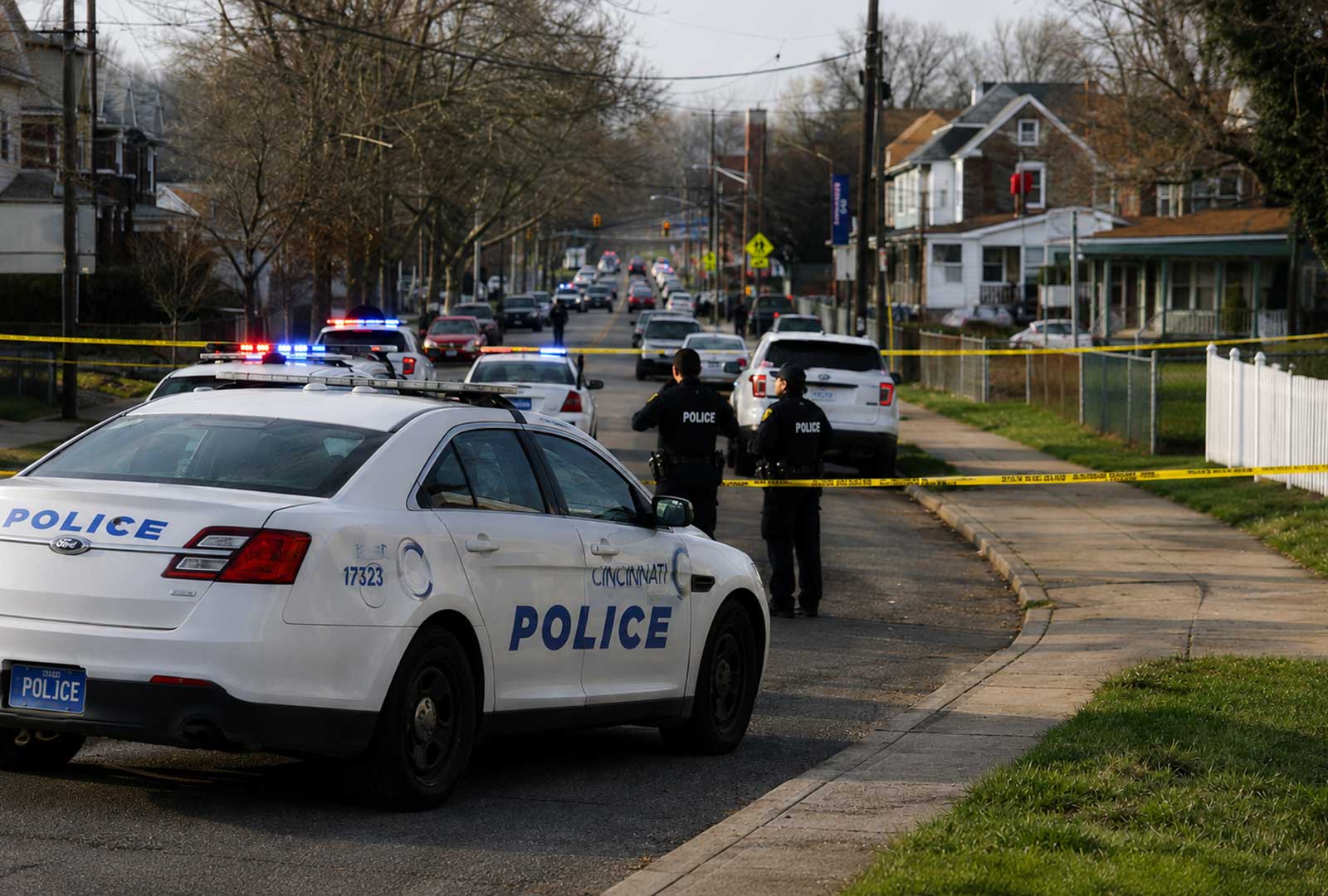 Cincinnati police officers and patrol vehicles block a residential street during a violent crime investigation as the city debates public safety, gun violence, and police staffing levels.