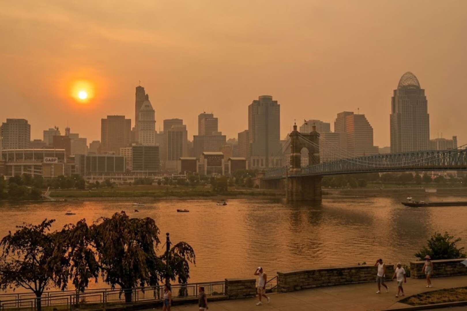 Hazy Cincinnati skyline at sunset during the June 2026 heat wave, viewed from across the Ohio River with the Roebling Suspension Bridge visible.