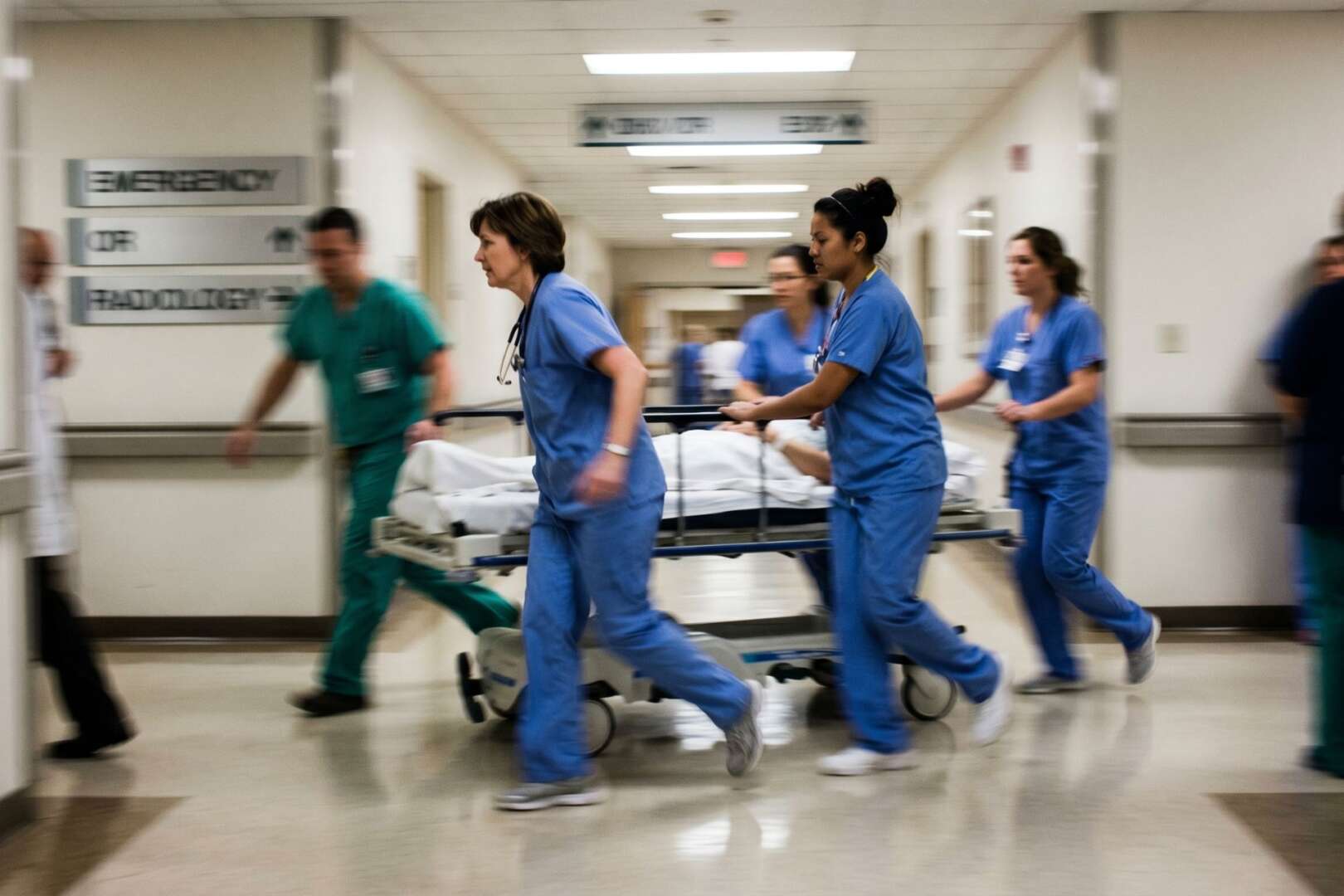 Medical professionals in scrubs urgently rushing a patient on a gurney down a hospital corridor.