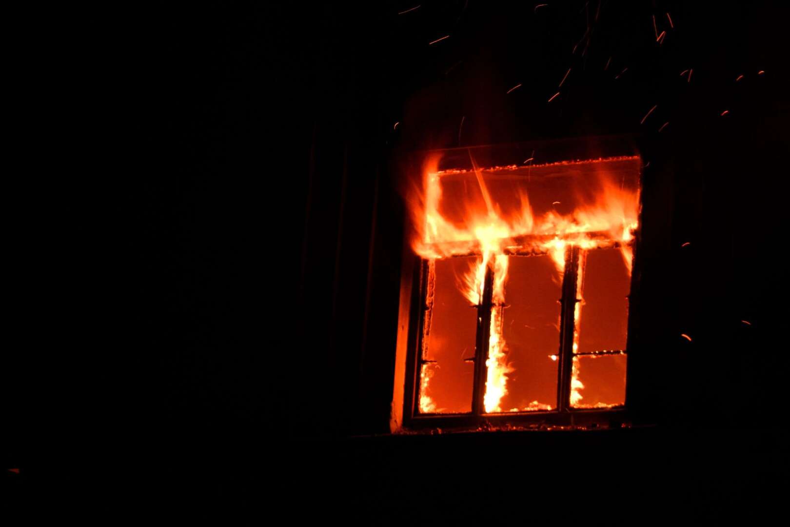 Bright orange flames blazing through the windows of a dark building at night.