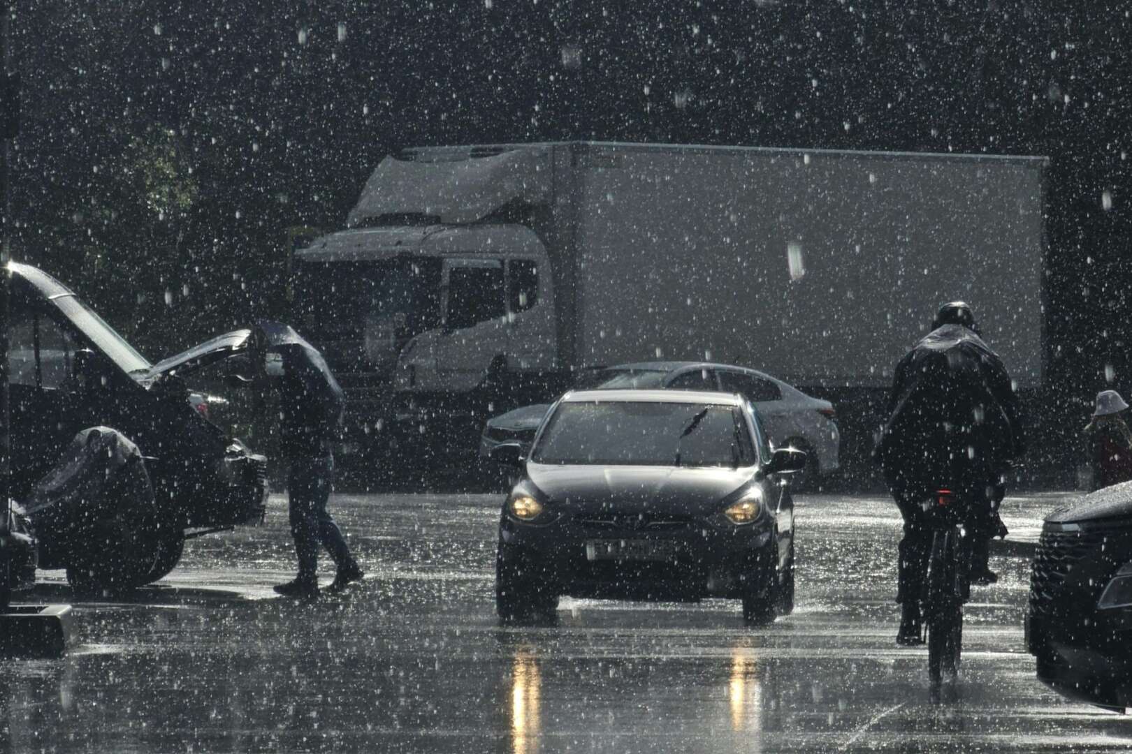 People walking and cycling through a heavy downpour and flooded streets next to vehicles in Cincinnati.