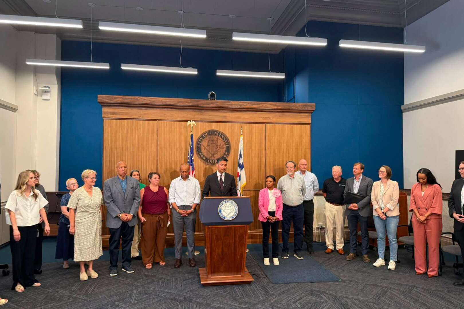 A group of city officials and community leaders standing behind a podium during a press conference regarding homeless services at the Cincinnati Center of Care.