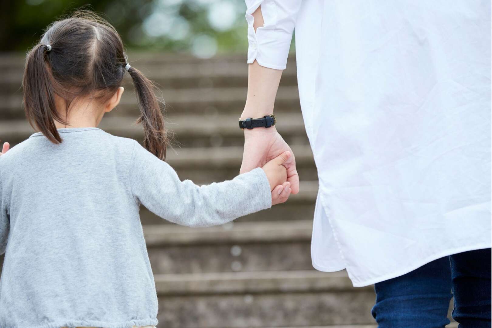 Two young children holding hands while walking outdoors in a park.