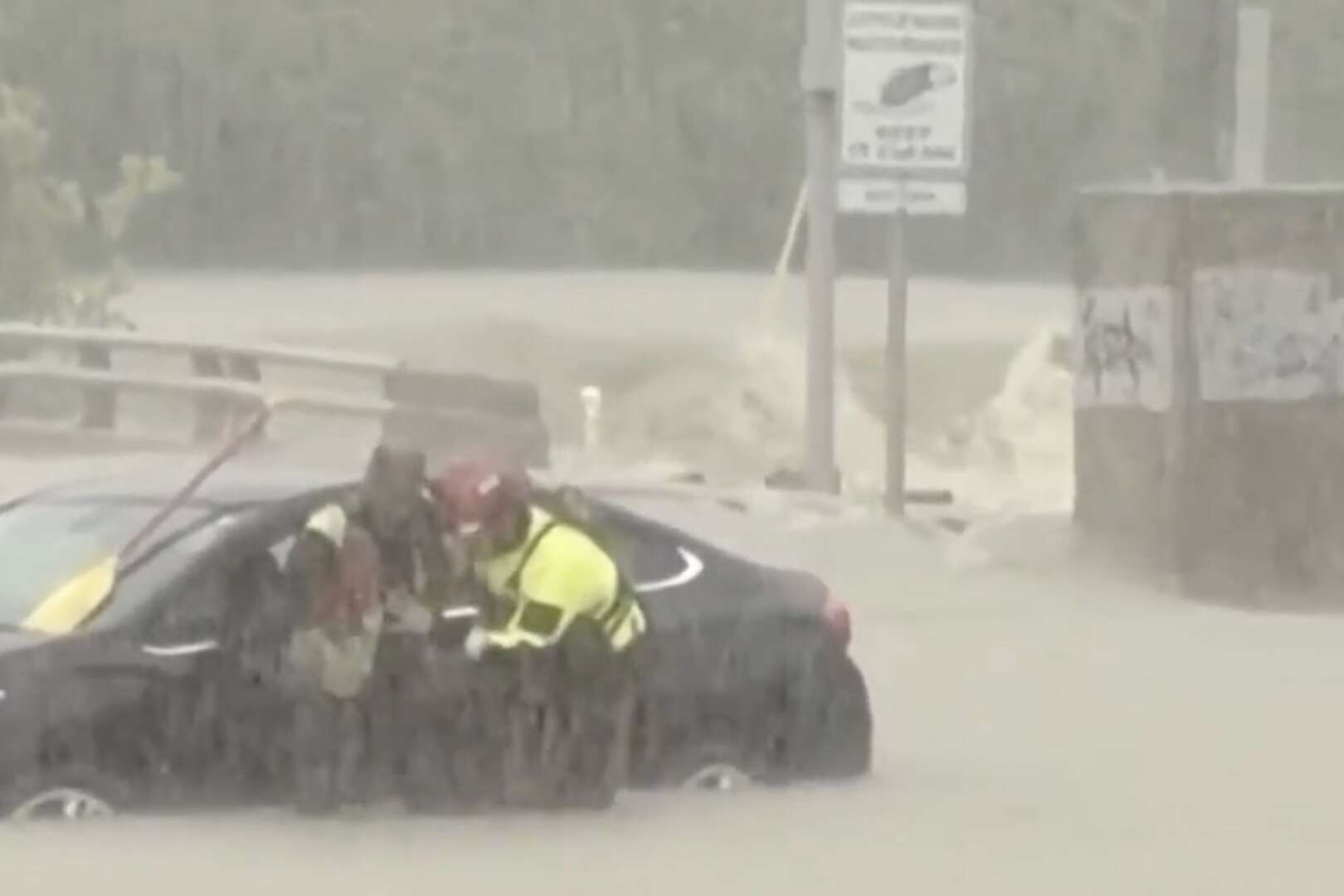 First responders in high-visibility jackets assisting a driver in a car partially submerged in floodwaters during heavy rain in Cincinnati.