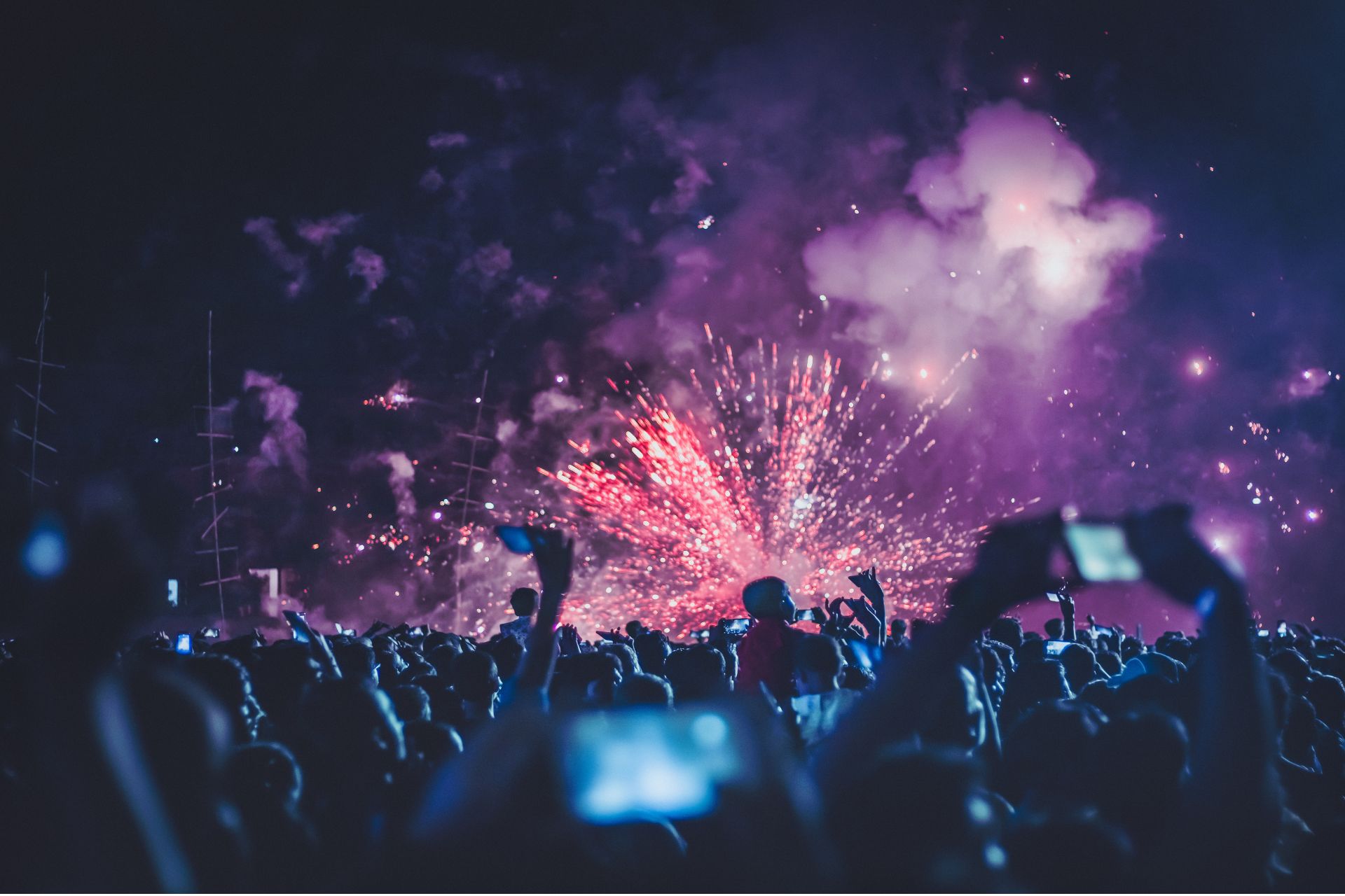 Crowd of attendees raising hands and glowing phones under vibrant stage lights at the Cincinnati Music Festival.